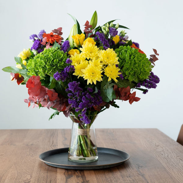 A large seasonal bouquet of flowers placed in a vase and shown on a dining room table 