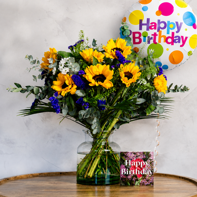 Bouquet of flowers with a 'Happy Birthday' balloon and card on a wooden surface.