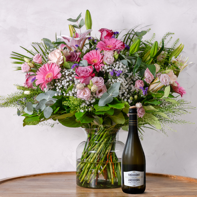 Bouquet of flowers in a vase with a bottle of wine on a wooden surface.