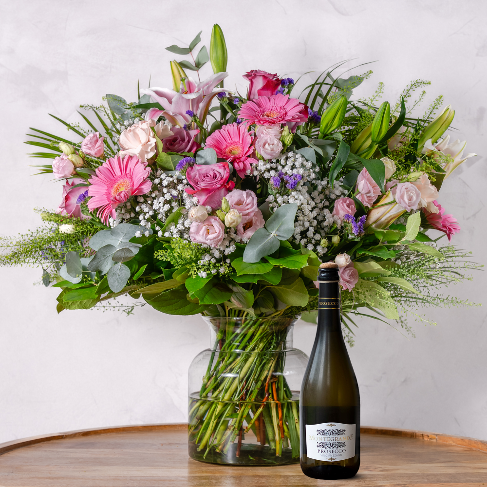Bouquet of flowers in a vase with a bottle of wine on a wooden surface.