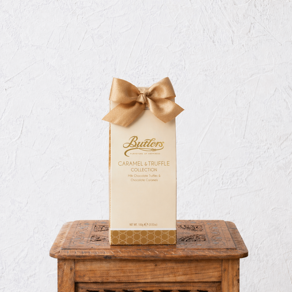 Butlers Caramel & Truffle Collection packaging with a gold bow on a wooden table against a white wall.