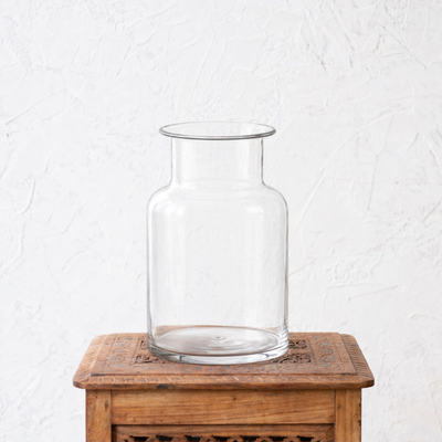 Clear glass vase on a wooden table with a white textured background