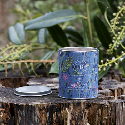 A white tin scented candle with 'IRISH BOTANICALS' branding next to its box, which has floral patterns and the product name 'BLOOMING BLUEBELL'.