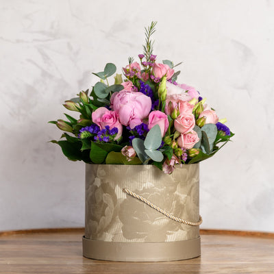 Floral arrangement in a decorative box on a wooden surface with a light background