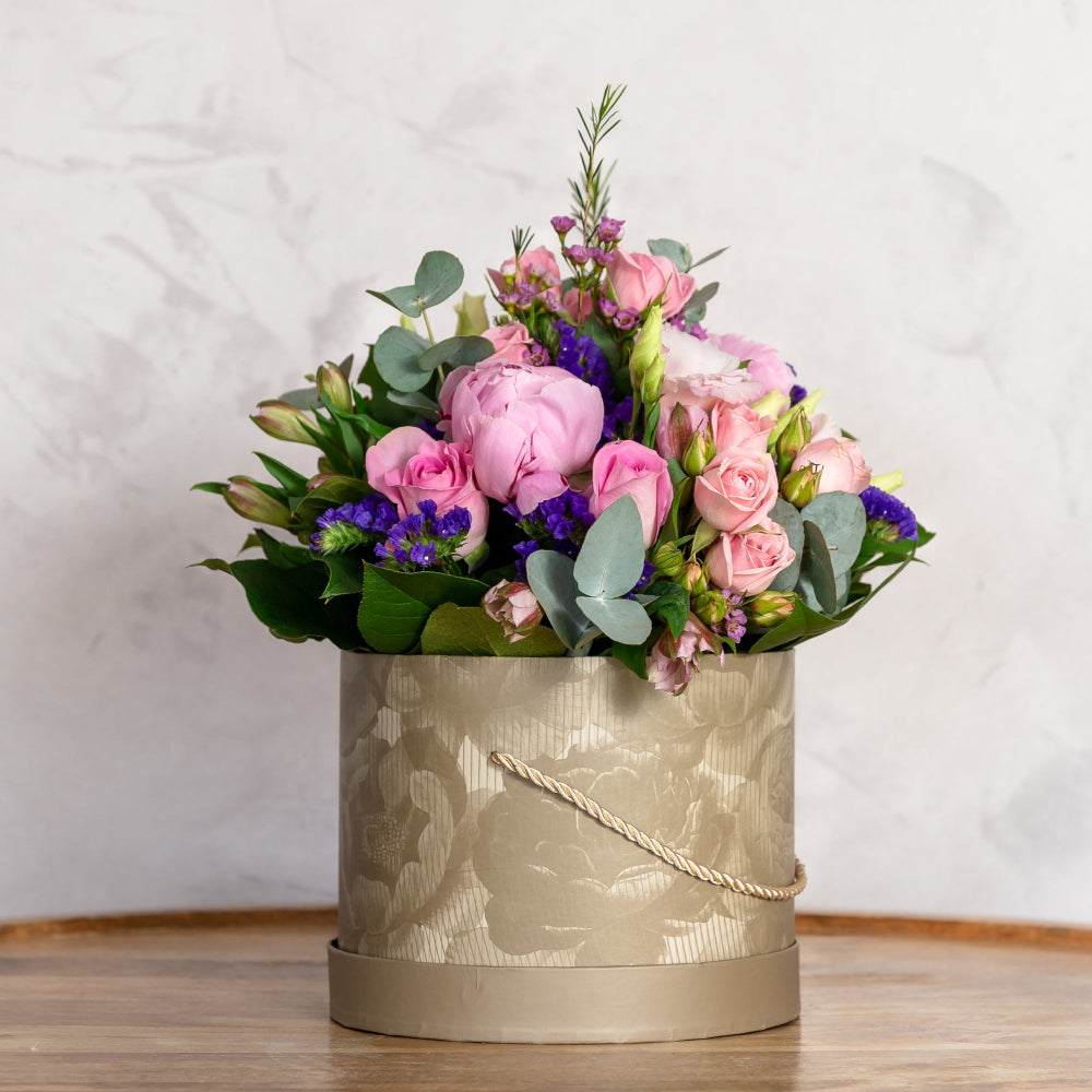 Floral arrangement in a decorative box on a wooden surface with a light background