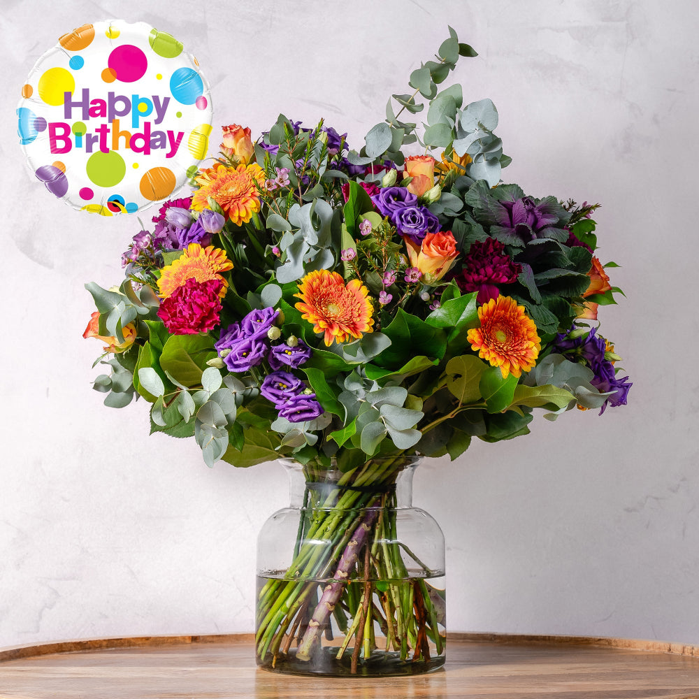 Bouquet of colorful flowers in a clear vase with a 'Happy Birthday' balloon on a white background
