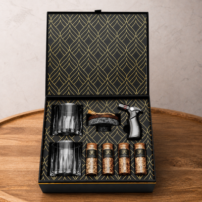 Set of glass tumblers, a brush, and bottles in a decorative box on a wooden surface.