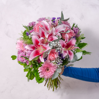 a bouquet of pink lilies, gerbera, roses hand-tied and being held from the side of the image 