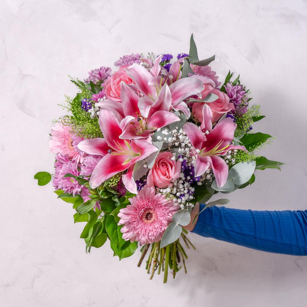 a bouquet of pink lilies, gerbera, roses hand-tied and being held from the side of the image 