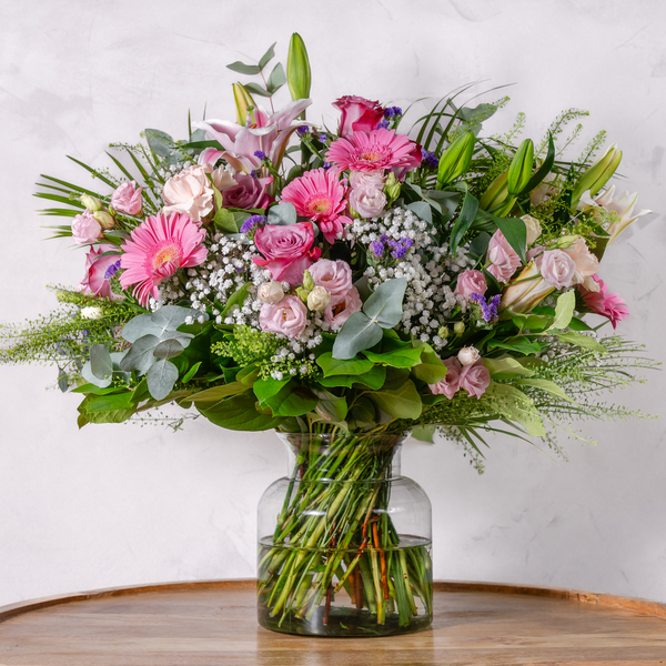 A vibrant bouquet of handpicked large-headed roses, lilies, and gerberas in a mix of pink, white, and green colors, arranged in a clear glass vase.
