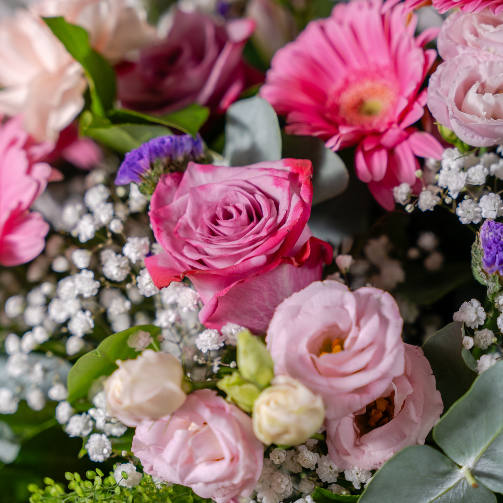 Close up showing the texture and detail of blush pink large-headed roses sitting alongside open white lily blooms and deep pink gerbera