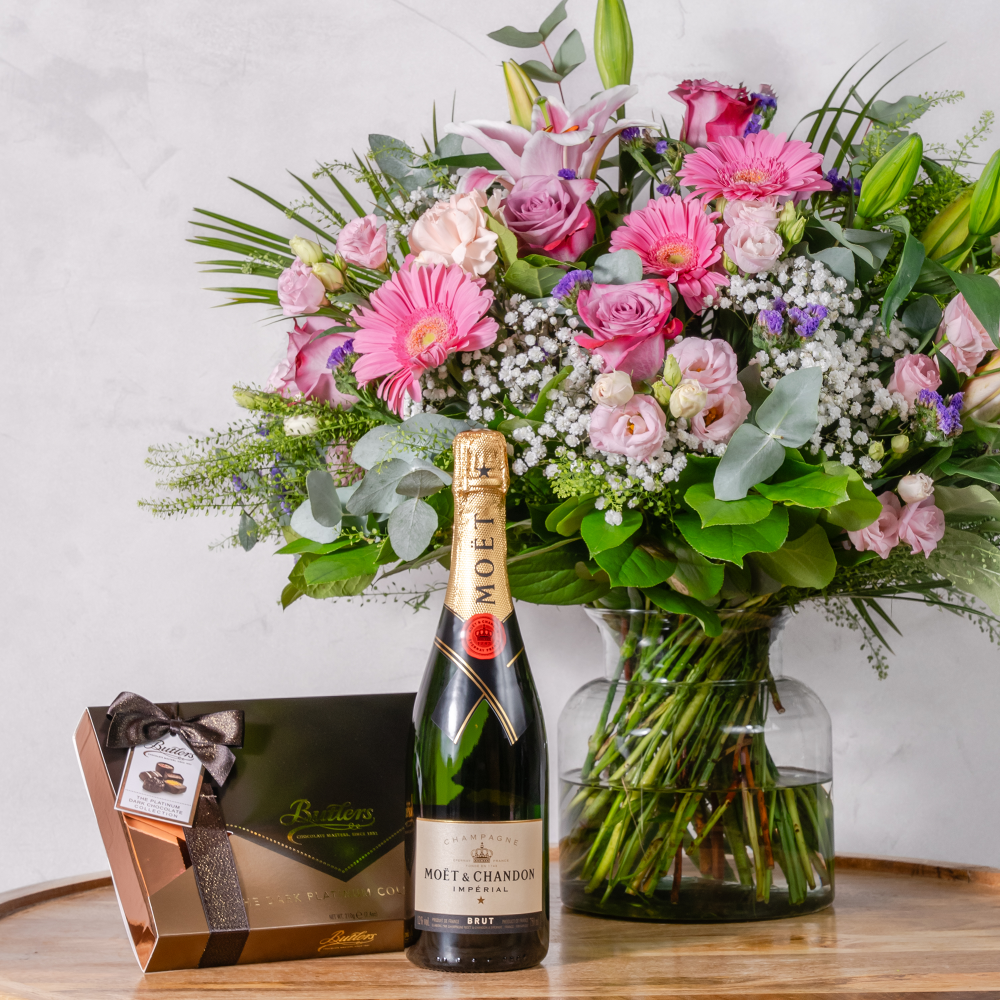 An elegant gift hamper arrangement featuring a bouquet of fresh flowers, a bottle of Moét & Chandon, and a selection of gourmet chocolates.