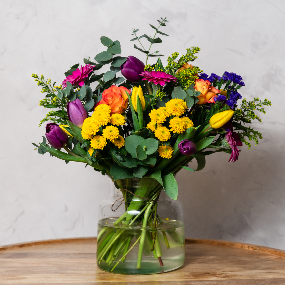 A colorful bouquet of flowers including tulips, roses, and eucalyptus, arranged in a clear vase.