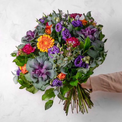 A vibrat seasonal bouquet full of deep colours hand-tied being held by a hand