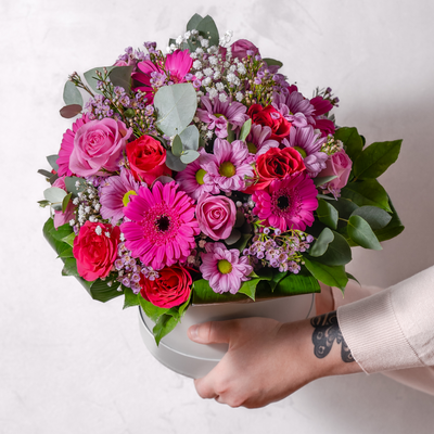 Fresh pink flowers in a hatbox being held by a pair of hands from the side 
