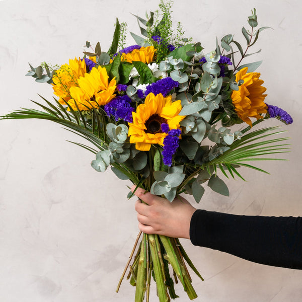 A bouquet of Sunflowers and statice being held upright by a hand 